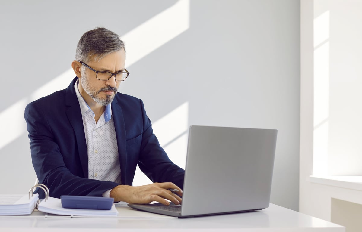 Business owner calculating company finances at a desk with calculator and laptop